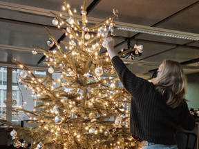 Mitarbeiterin, die eine Maske trägt, schmückt den Indoor-Weihnachtsbaum